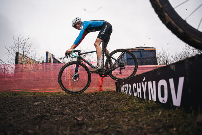A rider runs up the stairs with the bike by the Město Chýnov banner